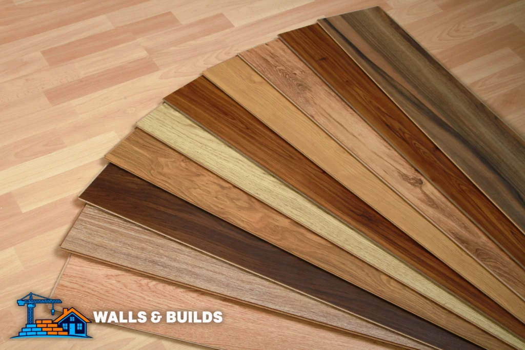 Stacked wooden floorboard planks in various finishes and wood tones, fanned out on a light-colored floor surface.
